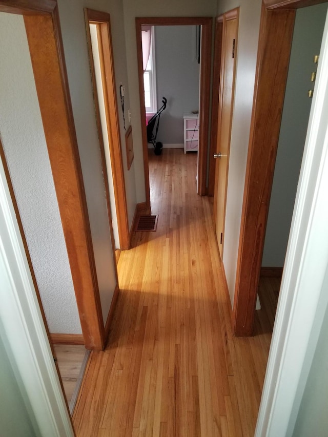 corridor featuring light wood-type flooring, visible vents, and baseboards