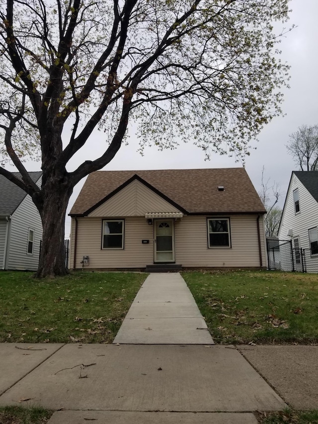 view of front of house featuring fence, a front lawn, and roof with shingles