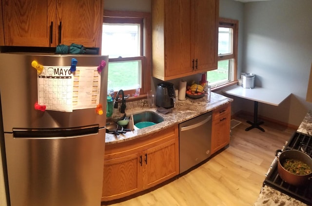 kitchen featuring appliances with stainless steel finishes, a wealth of natural light, light wood-style floors, and a sink