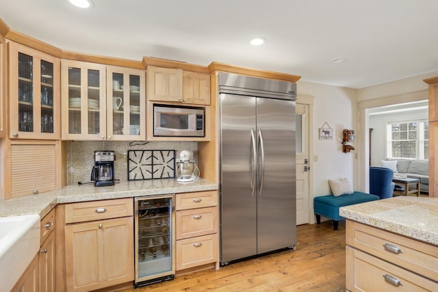 kitchen featuring built in appliances, light brown cabinetry, wine cooler, and light countertops