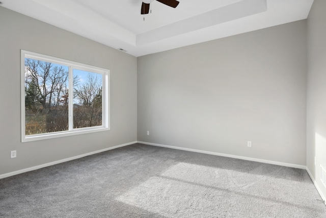 spare room featuring carpet, a raised ceiling, visible vents, ceiling fan, and baseboards