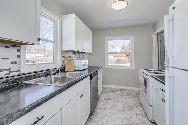 kitchen featuring white appliances, a sink, white cabinets, dark countertops, and plenty of natural light