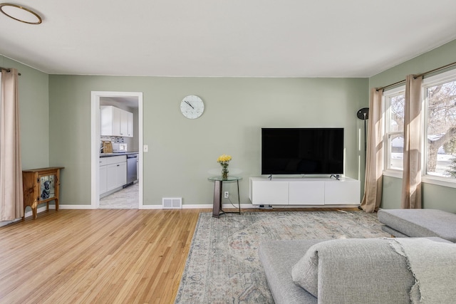 living room with visible vents, light wood-style flooring, and baseboards