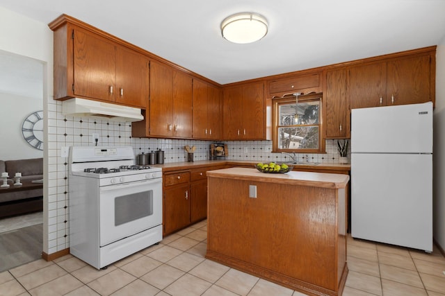 kitchen featuring white appliances, under cabinet range hood, brown cabinetry, and light countertops