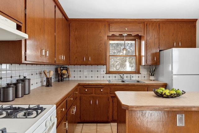 kitchen featuring brown cabinetry, freestanding refrigerator, ventilation hood, light countertops, and a sink