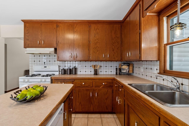 kitchen with white gas range oven, brown cabinetry, under cabinet range hood, a sink, and light tile patterned flooring