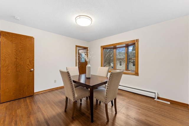 dining room featuring a baseboard heating unit, a textured ceiling, wood finished floors, and baseboards