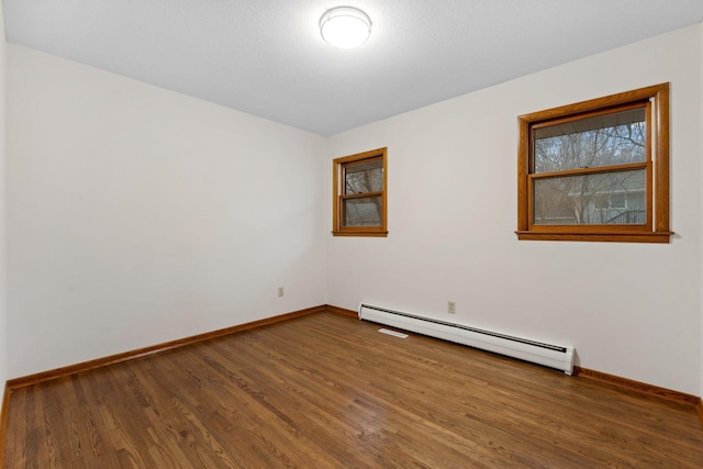 empty room featuring a baseboard heating unit, baseboards, and wood finished floors