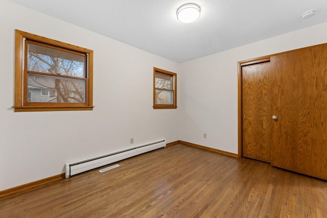 unfurnished bedroom with a baseboard radiator, multiple windows, baseboards, and wood finished floors