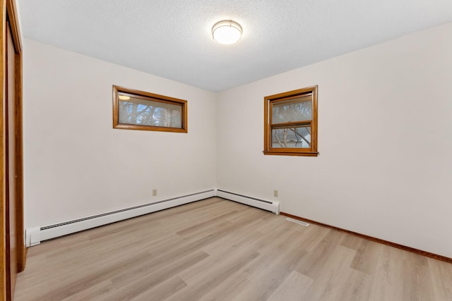 spare room featuring a textured ceiling, baseboard heating, light wood-style flooring, and baseboards