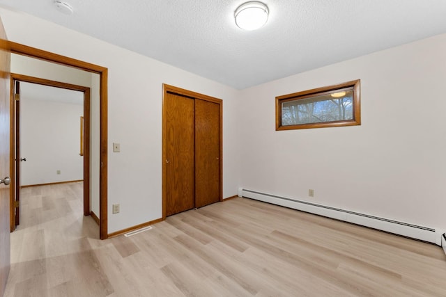 unfurnished bedroom with light wood finished floors, baseboards, baseboard heating, a textured ceiling, and a closet