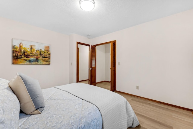 bedroom featuring light wood-style flooring, baseboards, and a textured ceiling