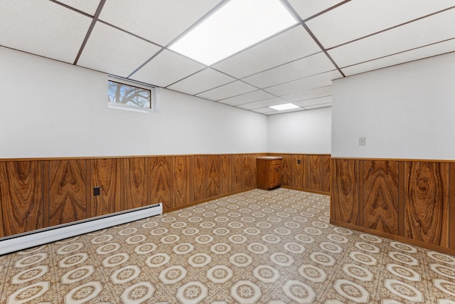 basement with wood walls, baseboard heating, wainscoting, and a paneled ceiling