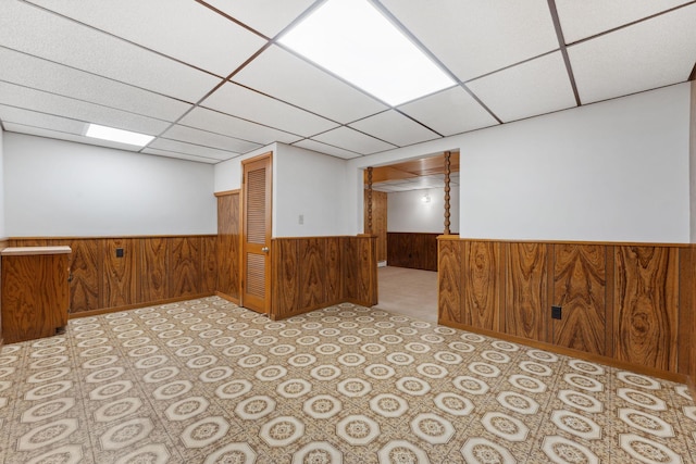 unfurnished room featuring a wainscoted wall, wooden walls, and a drop ceiling