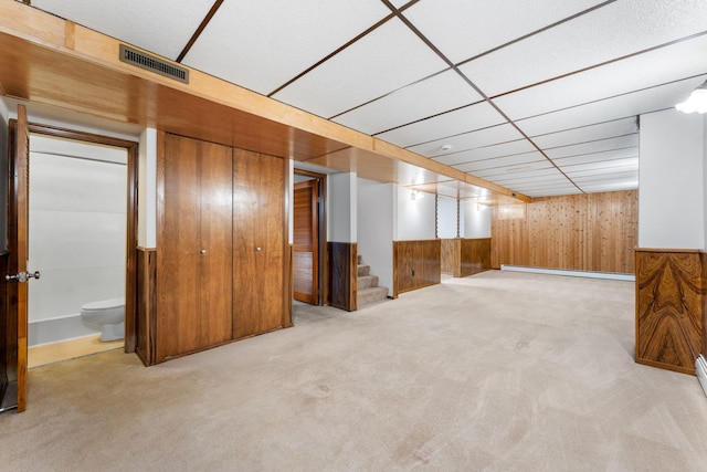 finished basement with a baseboard radiator, carpet, visible vents, and stairs