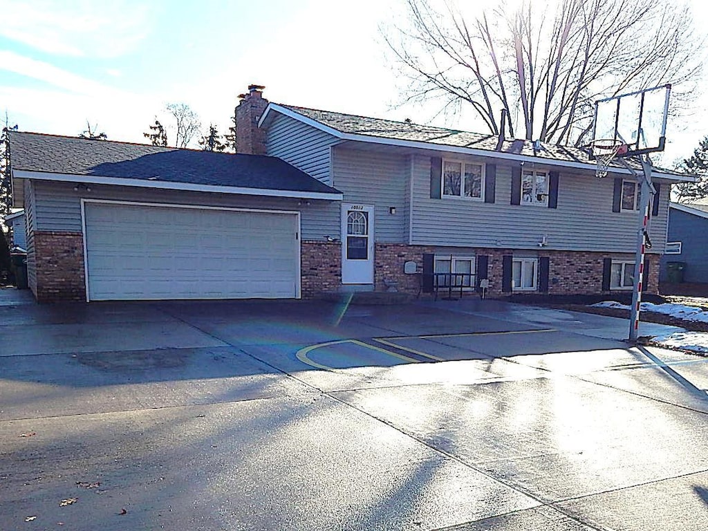 view of front of property featuring a garage, a chimney, concrete driveway, and brick siding