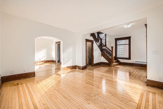 spare room featuring stairs, arched walkways, baseboard heating, and hardwood / wood-style floors