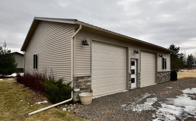 view of side of home featuring a garage, stone siding, and an outbuilding