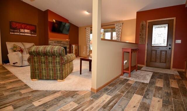 foyer entrance featuring lofted ceiling, a fireplace, baseboards, and wood finished floors