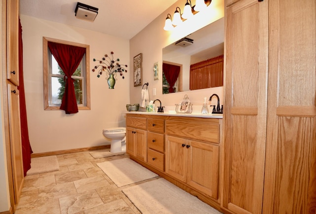 bathroom with double vanity, a sink, toilet, and baseboards