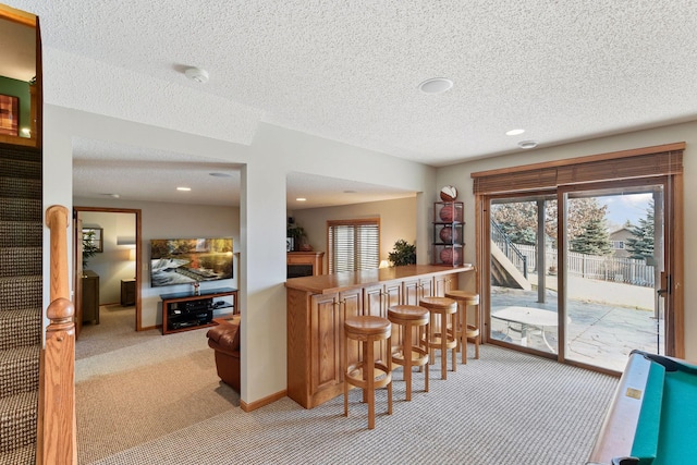 kitchen with a fireplace, a kitchen bar, light carpet, a textured ceiling, and baseboards