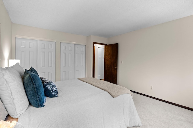 carpeted bedroom featuring two closets and baseboards