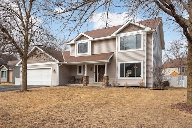 traditional-style home with a porch, an attached garage, fence, driveway, and a front lawn