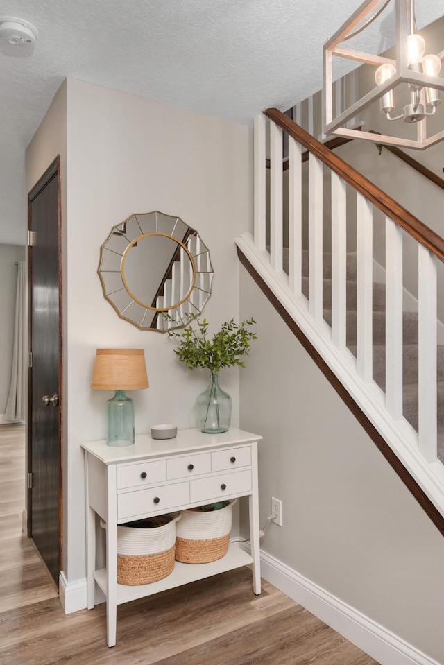 staircase featuring baseboards, a textured ceiling, a chandelier, and wood finished floors