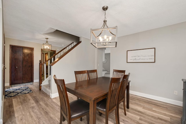 dining space featuring light wood finished floors, stairway, an inviting chandelier, and baseboards