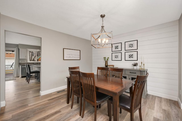 dining space with light wood-style floors, baseboards, visible vents, and an inviting chandelier