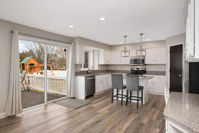 kitchen with white cabinets, appliances with stainless steel finishes, wood finished floors, a center island, and recessed lighting