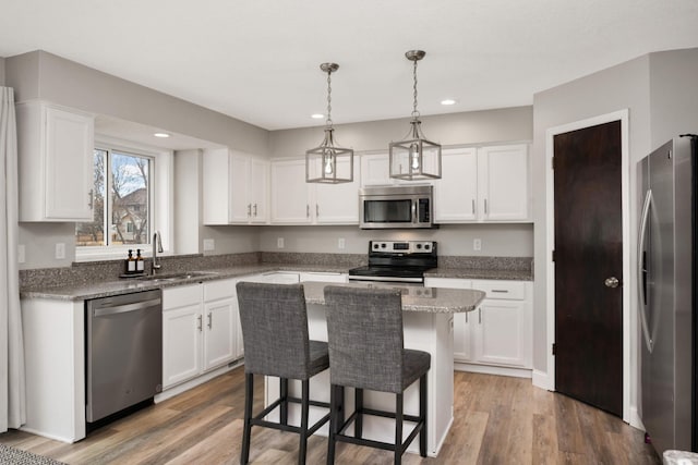 kitchen with appliances with stainless steel finishes, white cabinetry, a sink, and wood finished floors