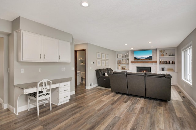 living area with baseboards, wood finished floors, a brick fireplace, built in shelves, and built in desk