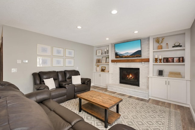 living room featuring light wood finished floors, a fireplace, recessed lighting, and built in features