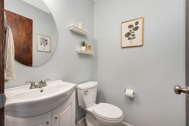 half bath with baseboards, vanity, and toilet