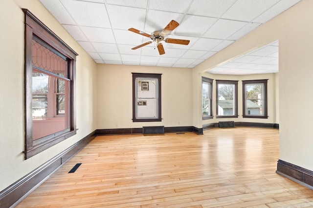 unfurnished room with a paneled ceiling, light wood-style flooring, visible vents, and baseboards