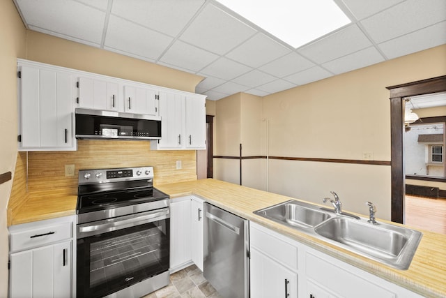 kitchen featuring decorative backsplash, appliances with stainless steel finishes, light countertops, a paneled ceiling, and a sink