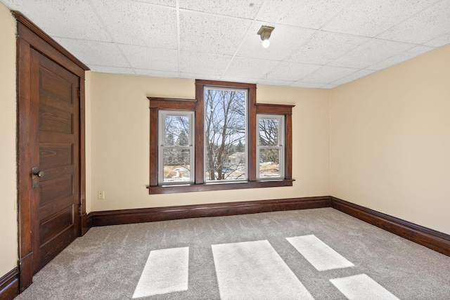 spare room with baseboards, a drop ceiling, and carpet flooring