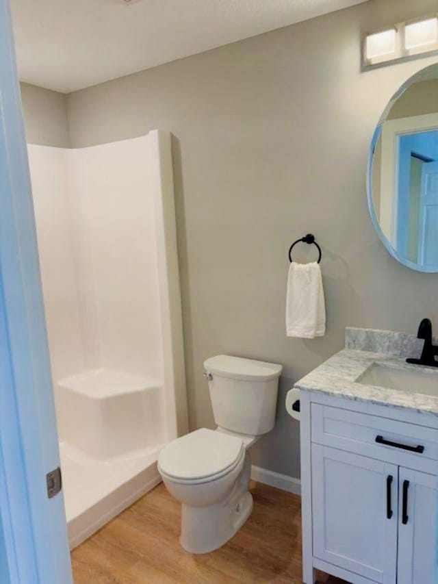 bathroom featuring toilet, a stall shower, wood finished floors, baseboards, and vanity