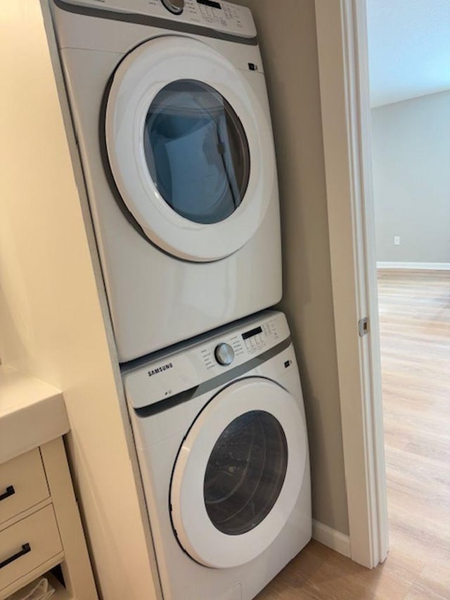 laundry room with laundry area, stacked washer / dryer, baseboards, and light wood finished floors