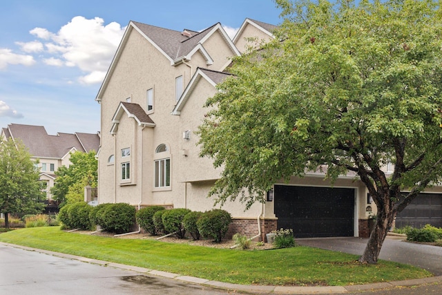 view of front of home featuring driveway, a garage, stucco siding, a front lawn, and brick siding