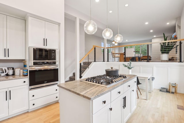 kitchen with a center island, white cabinets, appliances with stainless steel finishes, light wood-type flooring, and light stone countertops