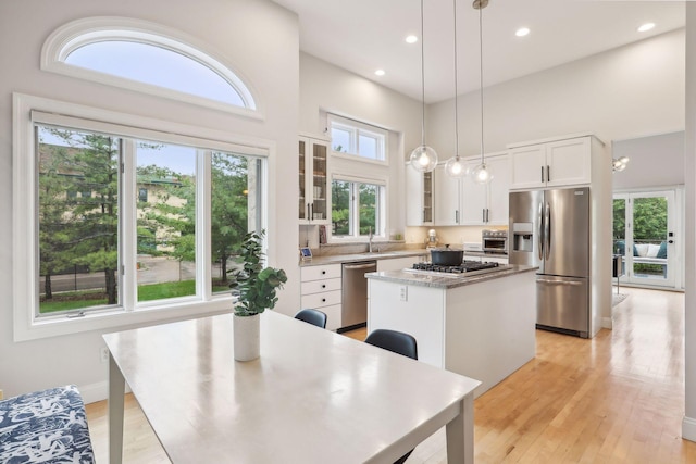 kitchen with appliances with stainless steel finishes, glass insert cabinets, white cabinetry, a kitchen island, and a sink