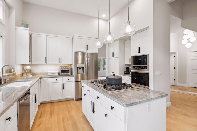 kitchen featuring a kitchen island, a high ceiling, stainless steel appliances, light wood-style floors, and a sink