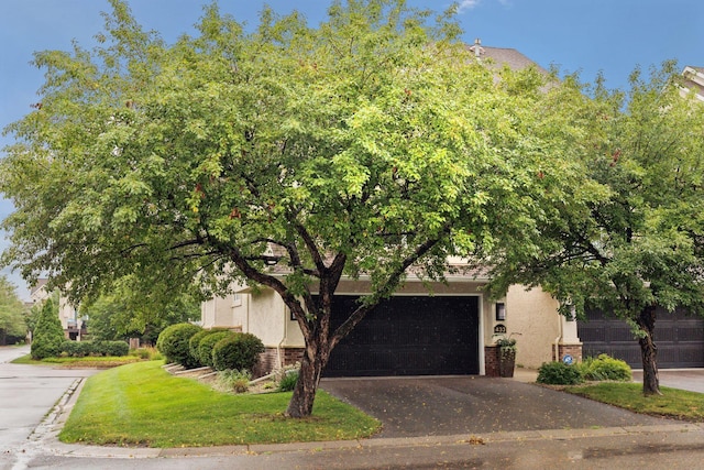 view of property hidden behind natural elements featuring a garage, stucco siding, aphalt driveway, and brick siding