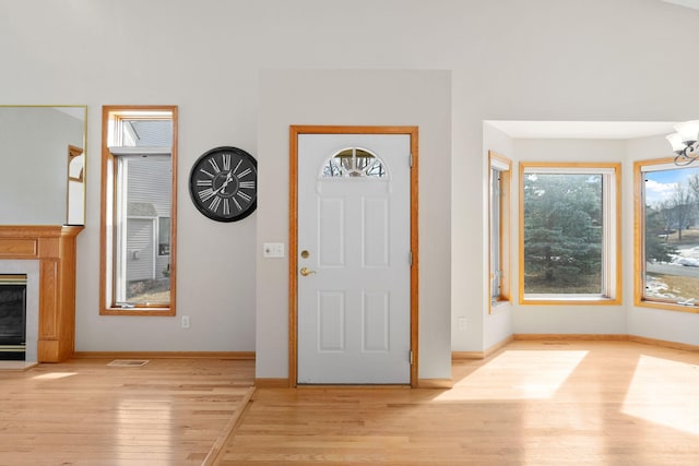 foyer featuring a notable chandelier, baseboards, light wood-style floors, and a high end fireplace