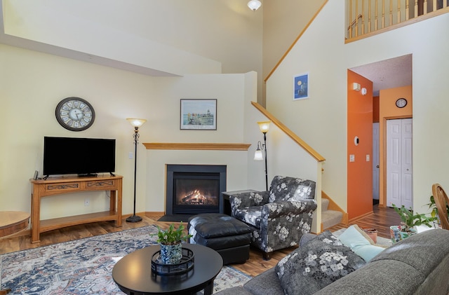 living room with a high ceiling, a fireplace with flush hearth, wood finished floors, baseboards, and stairs