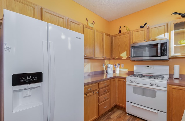 kitchen featuring white appliances, light wood finished floors, and a textured ceiling