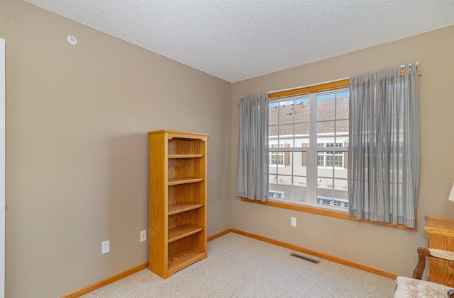 empty room featuring carpet, visible vents, a textured ceiling, and baseboards