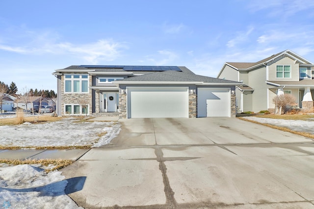 view of front of property with an attached garage, stone siding, driveway, and roof mounted solar panels